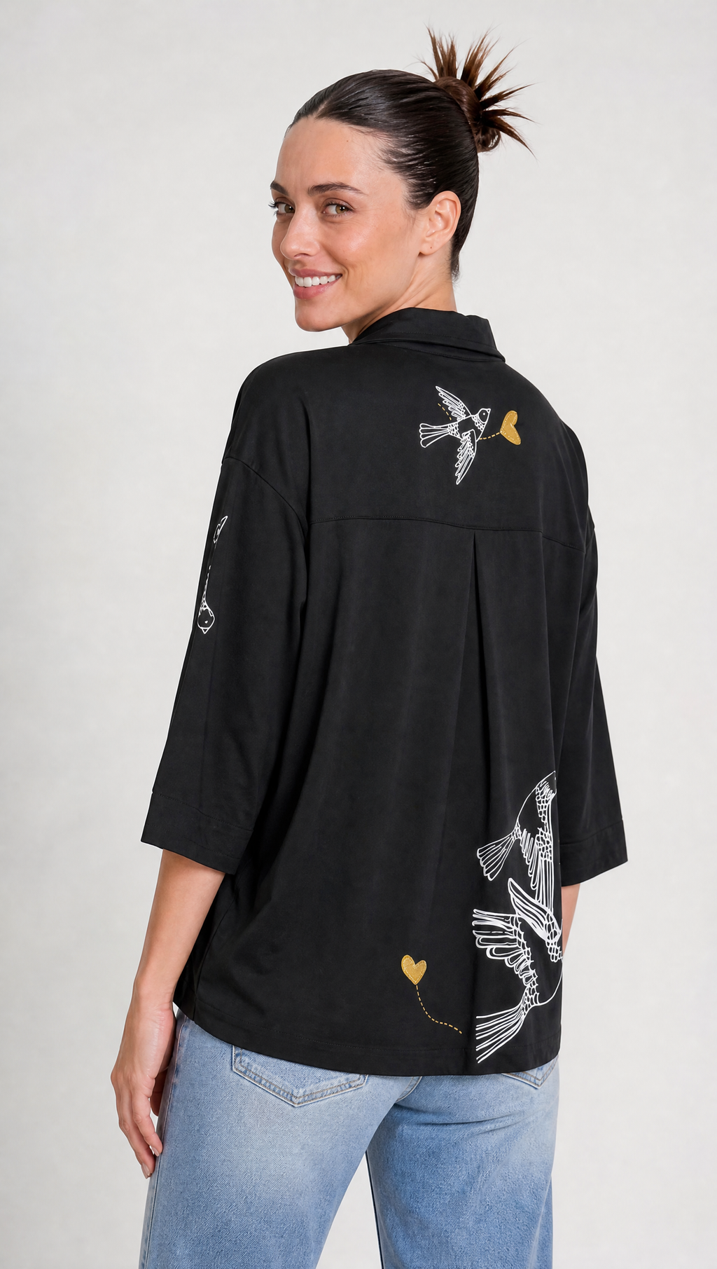 Aves y corazones en delicadas líneas doradas y blancas: el arte gráfico que transforma una camisa básica en una pieza de autor.