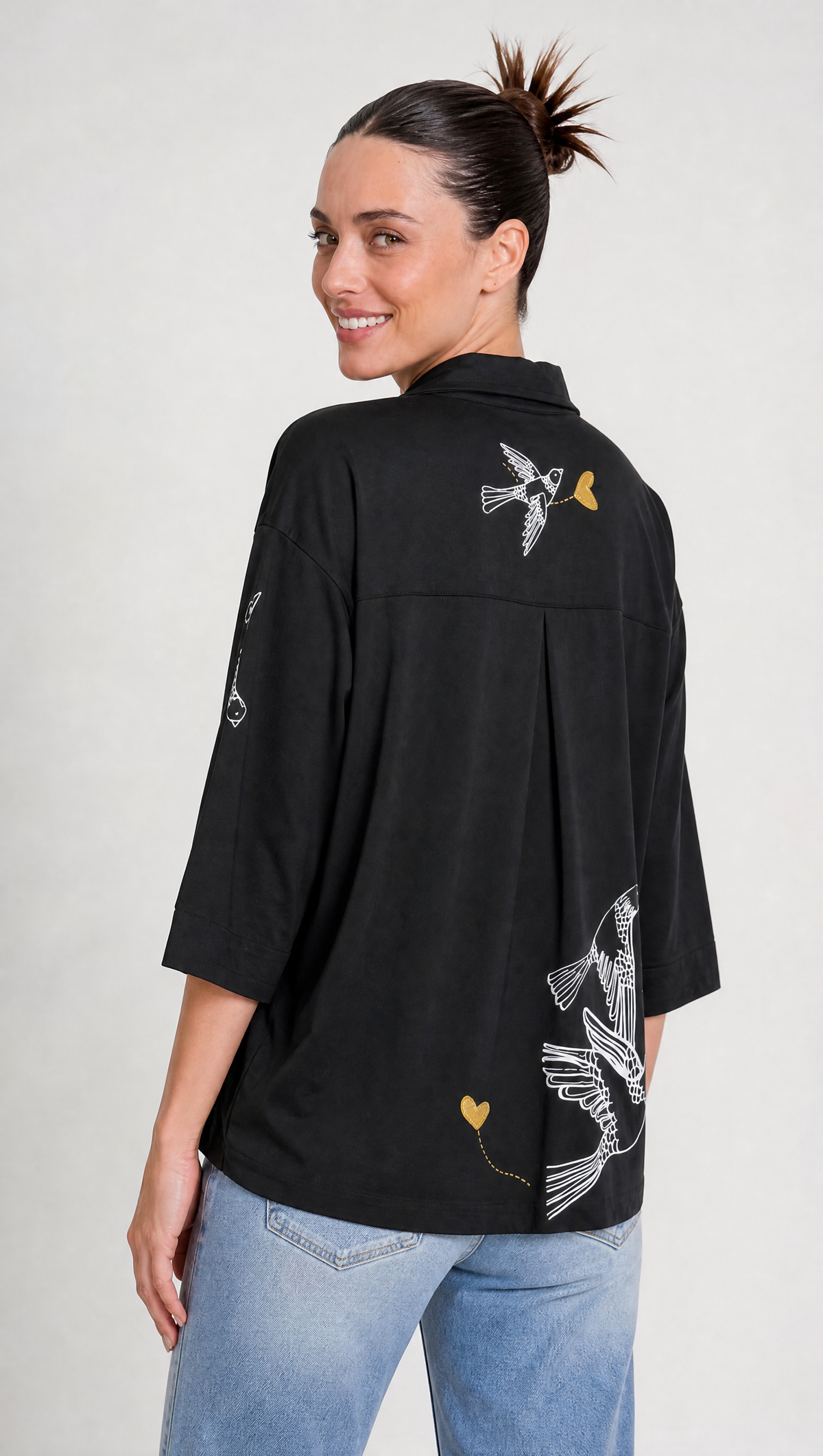 Aves y corazones en delicadas líneas doradas y blancas: el arte gráfico que transforma una camisa básica en una pieza de autor.
